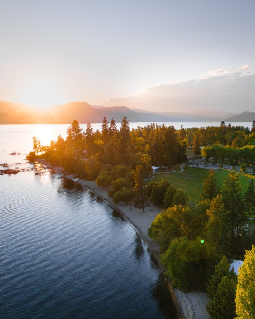 A drone captures Naramata beach glowing under an orange summer sunset in British Columbia