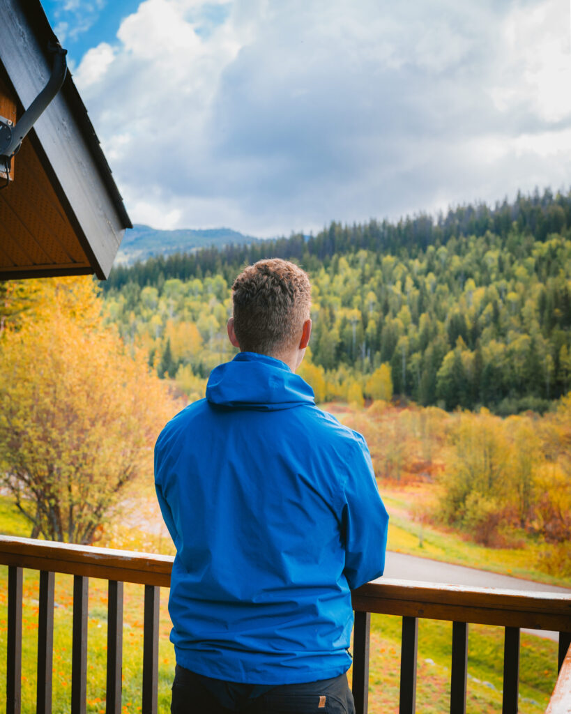 A man stands on the porch of a cabin at Alpine Meadows Resort British Columbia, looking out into the forest scenery