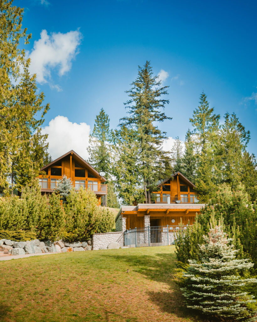 Two tall wooden cabins are peeking out from tall forested trees on a blue sky day at Alpine Meadows Resort British Columbia