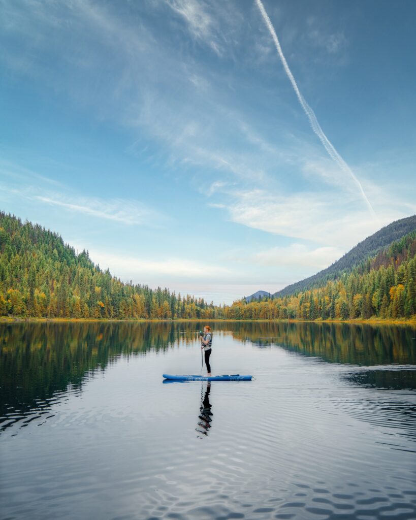 A girl stands on a paddle board on Halmore Lake at Alpine Meadows Resort near Wells Gray Provincial Park British Columbia
