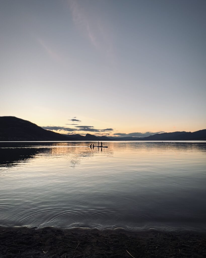 Friends paddle board on Okanagan Lake as the sun sets in Penticton, British Columbia