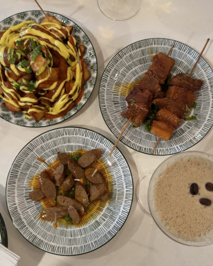 Various tapas plates and cocktails cover the table at Chulo Tapas Bar in Penticton, British Columbia. The plates include lamb sausage, pork belly, and fried potatoes.