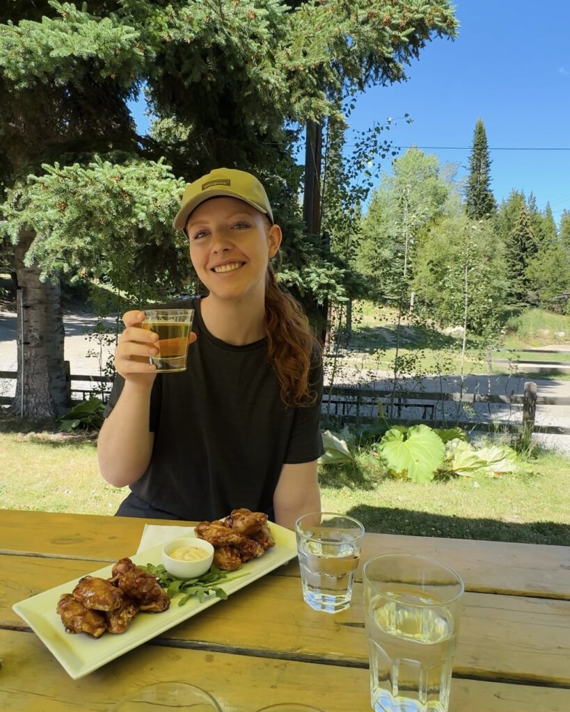 A girl holds up her beer as she enjoys a plate of chicken wings on a patio table at Chute Lake in Naramata, British Columbia