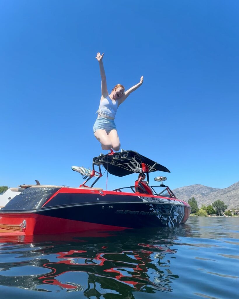 A girl jumps off of a boat with arms above her head into blue Osoyoos Lake