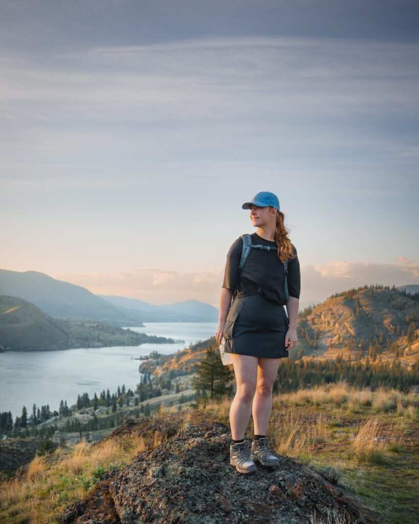 A girl standing on a rock at the summit of a hike in Okanagan Falls British Columbia. The valley and lake is covered in golden light.