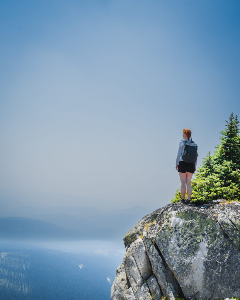 A girl stands on a rock looking out towards the Okanagan Valley from Big White in Kelowna, British Columbia