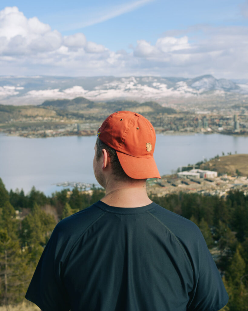 A man stands at the summit of Rose Valley looking towards Kelowna, British Columbia and the city skyline across the lake