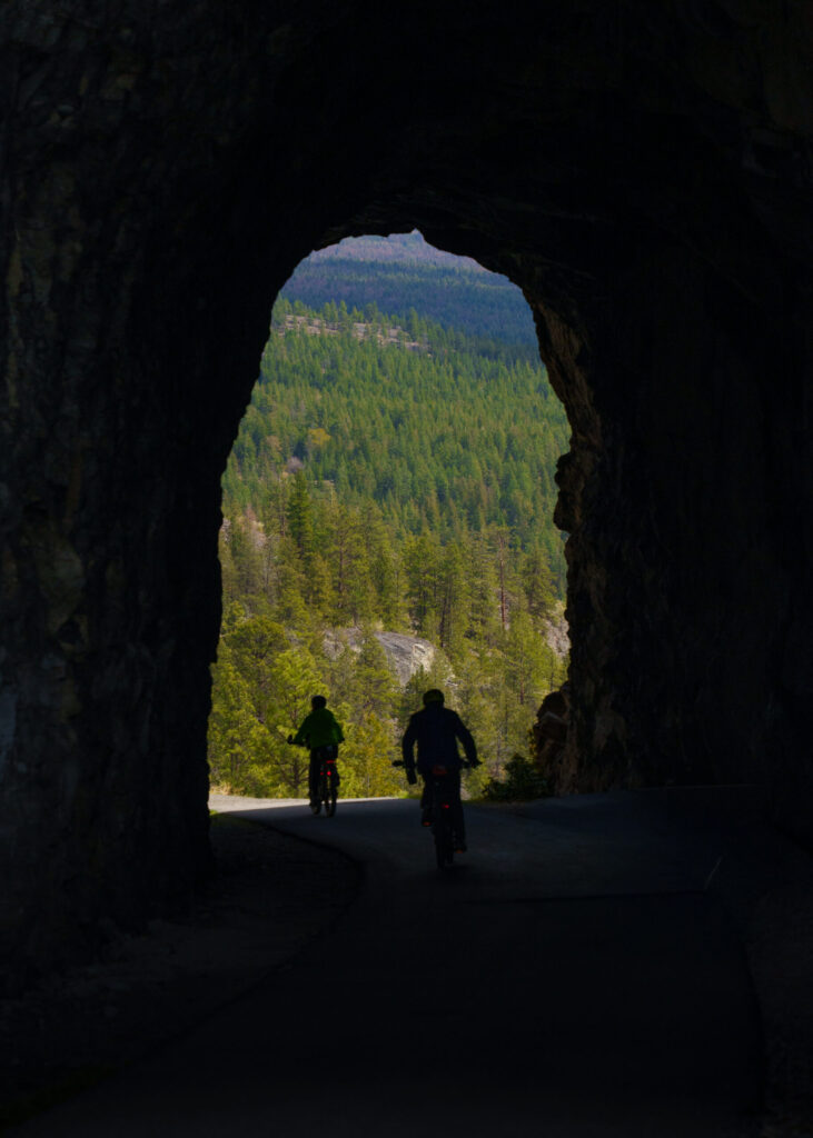2 bikers ride through the Little Tunnel in Naramata British Columbia heading towards Penticton