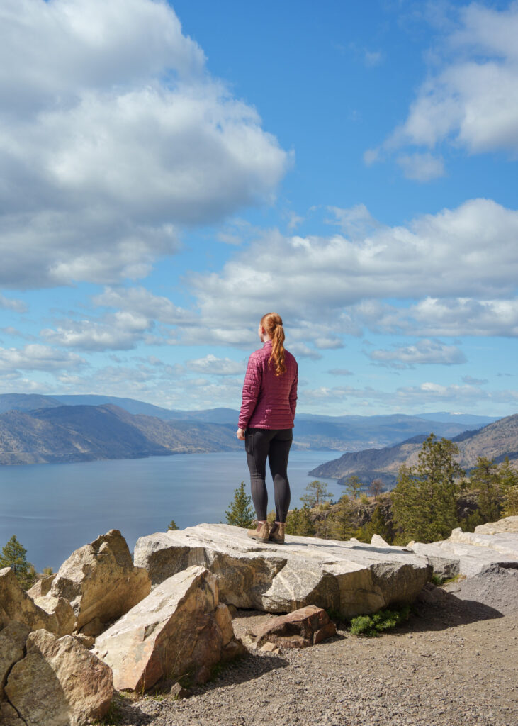 A girl stands on a rock looking out towards Okanagan Lake from The Little Tunnel on the KVR Trail in Naramata British Columbia