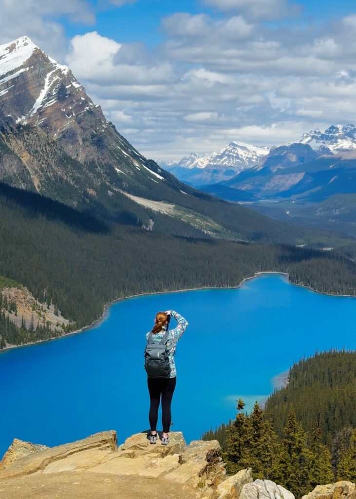 A woman stands on a rock taking a photo of Peyto Lake in Banff National Park